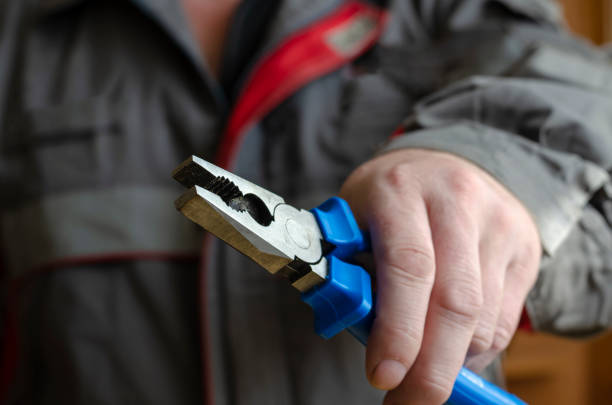 A man holds out the pliers into the camera. A man holds out the pliers into the camera. Mechanic in a red-gray working uniform with a tool in his hand. Close-up. Selective focus. Blurred background. pliers stock pictures, royalty-free photos & images