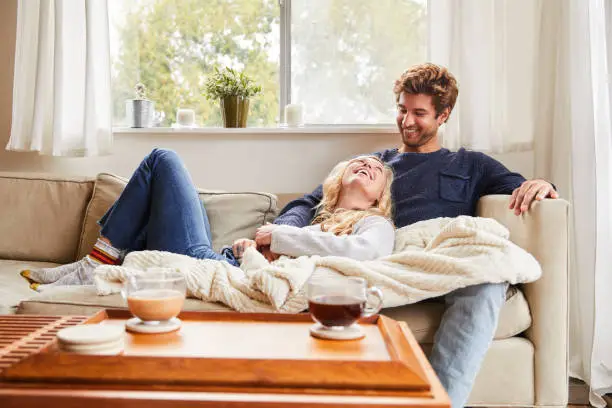 Smiling young woman talking with her boyfriend while relaxing together on their living room sofa at home