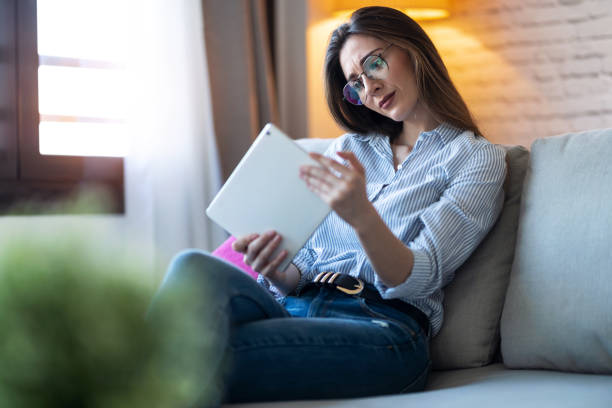 istock Concentrated young woman using her digital tablet while sitting on sofa at home. 1218766048