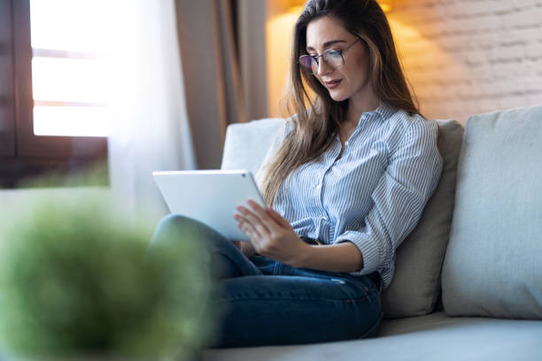 istock Pretty young woman using her digital tablet for reading while sitting on sofa at home. 1218766353