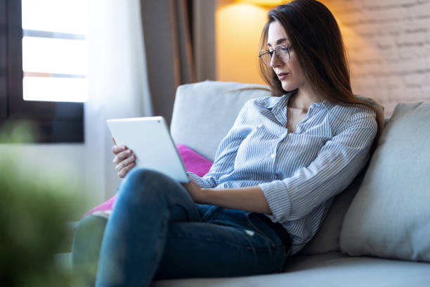 istock Pretty young woman using her digital tablet for reading while sitting on sofa at home. 1218766453