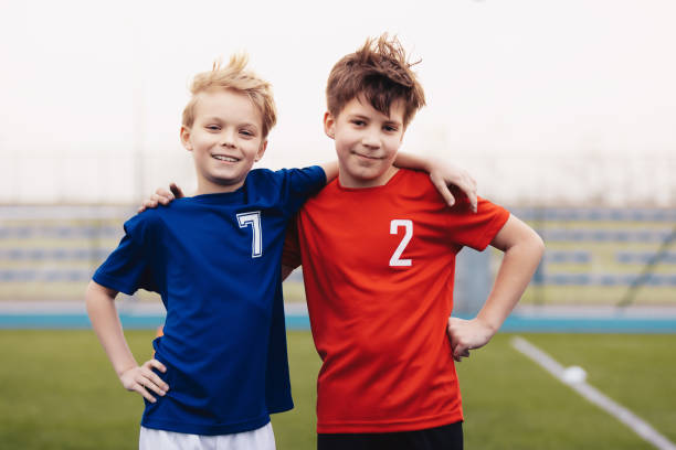 dos chicos felices al aire libre en ropa deportiva. niños sonriendo a la cámara. niños de pie en el campo de césped deportivo. educación deportiva para niños - team sport enjoyment horizontal looking at camera fotografías e imágenes de stock