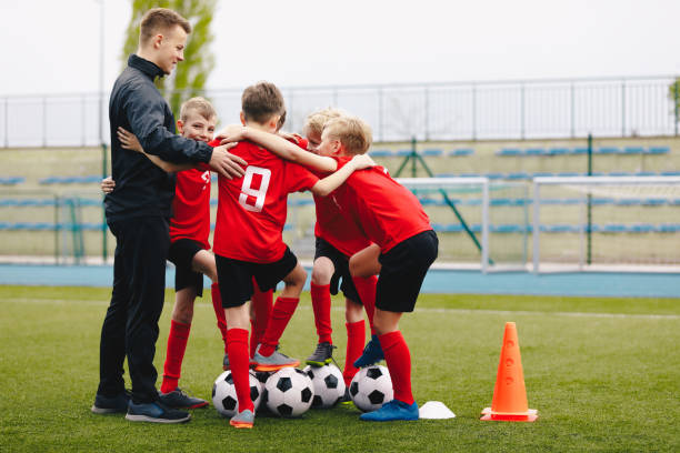 trainer gibt jungen fußball-team anweisungen. kinder sport team treffen. kinder spielen sport. jungen in sportuniformen mit shout team. jugendsport für kinder. junior level fußball hintergrund - soccer child coach childhood stock-fotos und bilder