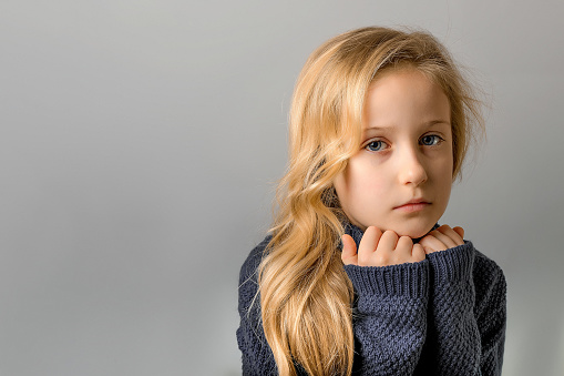 Color portrait of serious child girl, headshot portrait of sad little girl posing in studio