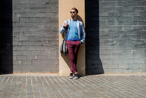 Young bearded man, model of fashion, in urban background wearing casual clothes while leaning on a office building wall