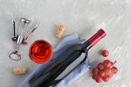 Bottle of wine, wine glass with wine, grapes and corkscrew on gray background with copy space for your text . Top view. Flat lay.