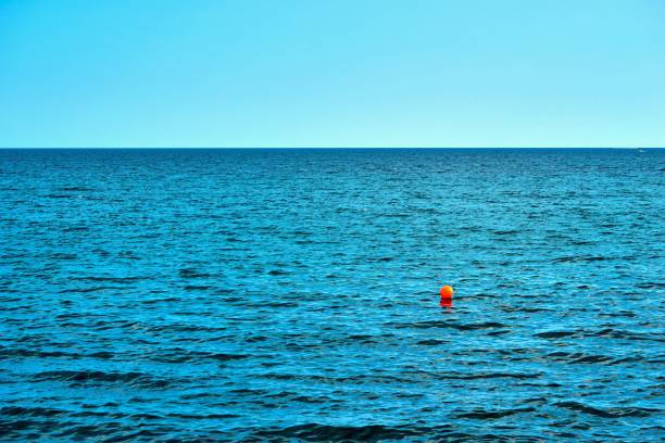 one small red ball or buoy in foreground in clear blue sea and the skyline in the background