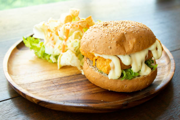 istock Fried fish fillet burger with vegetable salad on wood plate background 1218773915