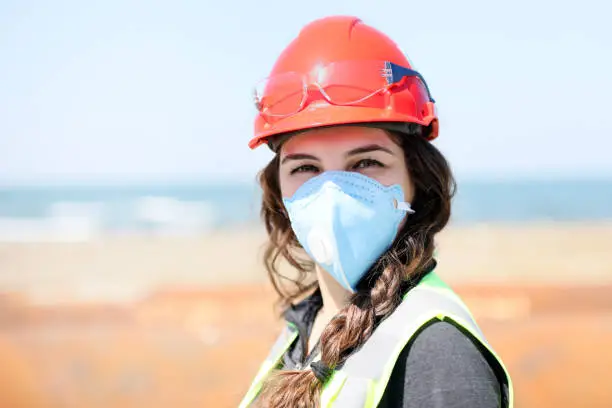 Occupational health and safety (OHS) woman staff (engineer) looking at the camera with protective mask for coronavirus (covid-19) in the construction field.