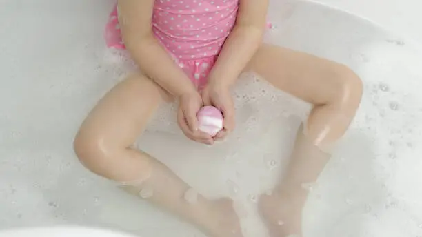 Photo of Hands of girl puts bath bomb to water. Ball of bath salt dissolves in water