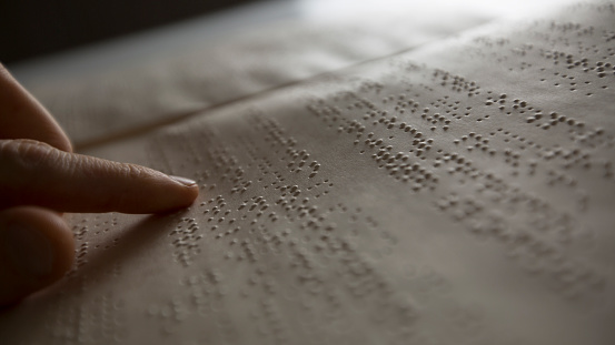 The hand of a blind man reads the text of a braille book.