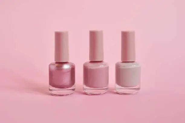 Still life shot of nail polish bottles against a pink background