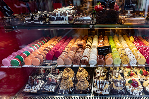 A variety of cakes in a cake shop window in the centre of Amsterdam, Netherlands. They include macarons (macaroons) and a variety of strawberry tarts.