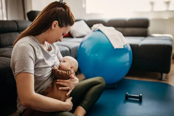 Photo of Mother taking a break from exercising to breastfeed her baby son at home