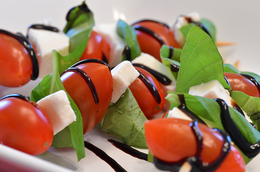 Tomato, basil, fresh mozzarella and balsamic glaze on wooden sticks. Close up of a fresh and healthy appetizer.