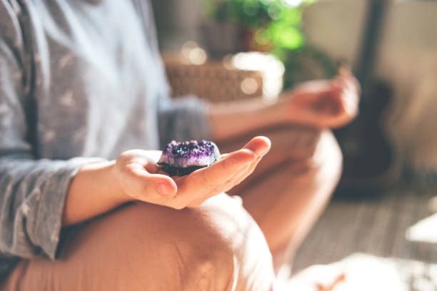 Young beautiful woman is meditating with a crystal in her hand. Young beautiful woman is meditating with a crystal quartz in her hand. Sits on the floor at home. crystal stock pictures, royalty-free photos & images