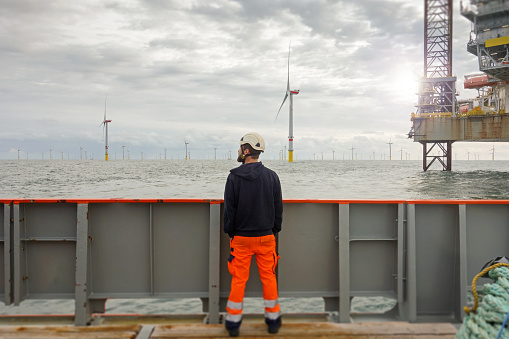 Technician standing on transfer vessel deck and in the morning and looking on offshore wind farm and offshore platform around in German north sea