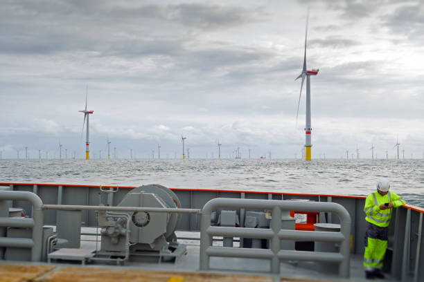 istock Technician standing on transfer vessel deck and checking mobile and offshore wind farm is behind 1218789563