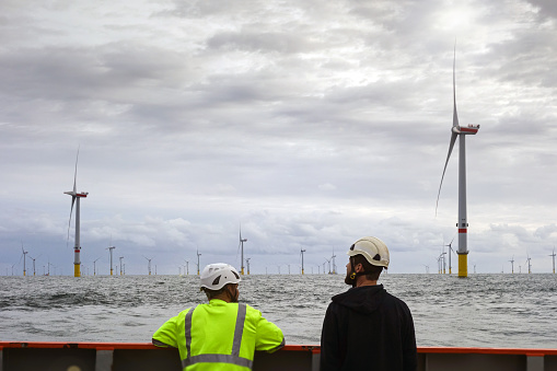 Two Technician standing on transfer vessel deck and in the morning and looking on offshore wind farm and offshore platform around in German north sea