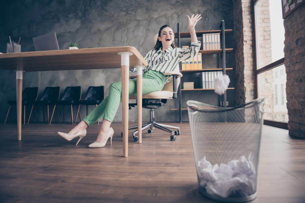 full-size-foto von positiven fröhlichen arbeiter vermarkter mädchen haben keine arbeit gefühl spaß werfen zerknitterten papier in mülleimer sitzen stuhl in modernen loft büro - man throwing papers stock-fotos und bilder