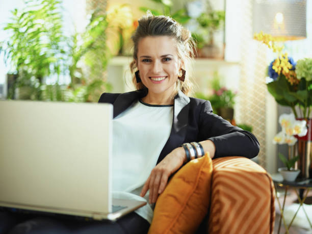 smiling woman typing message on laptop while sitting on sofa