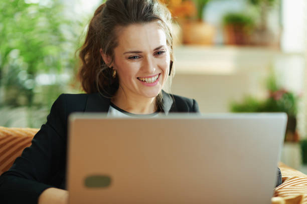 istock happy trendy woman using laptop while sitting on sofa 1218790117