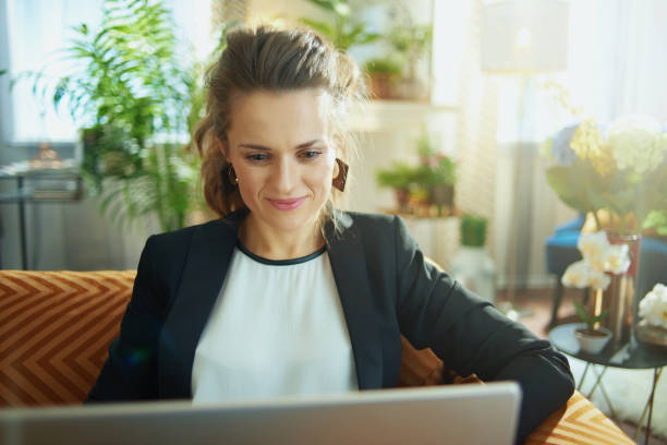istock happy housewife typing message on laptop while sitting on sofa 1218791279