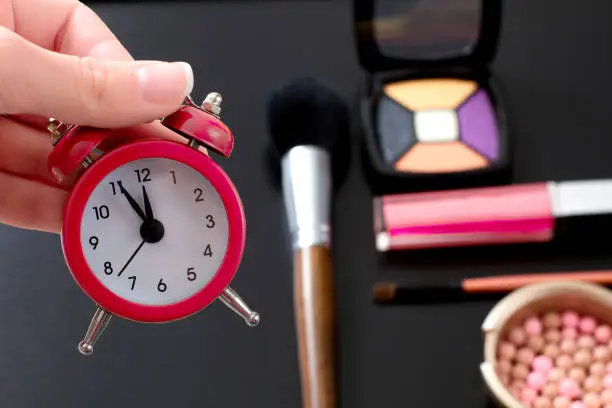 Photo of Concept cropped image with cosmetic and make up products. Quick make-up. Red retro clock. Selective focus