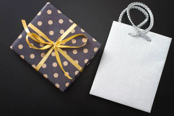 Photo of Gift box in polka dots and paper bag on black background. Top view and copy space