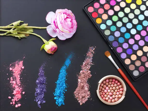 Photo of Makeup tools and accessories isolated on black background. Top view and mock up. eye shadows, make up brushes and decorative flower.