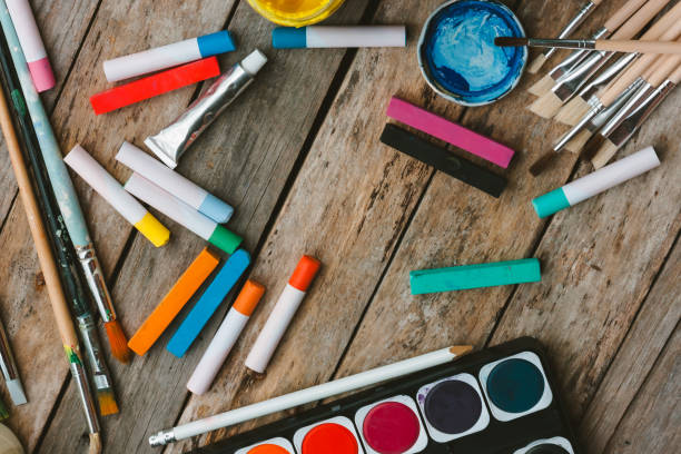 istock Artist paint brushes, chalks and watercolor paintbox on wooden background. Tools for creative leisure. Painting hobby background. Paintings art concept. Copy space. Top view 1218796492