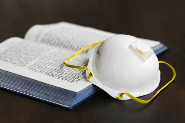 N95 Mask and hebrew prayerbook: pray indoors concept.