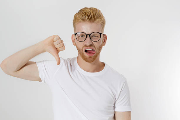 istock Dislike sign, hand gesture. Young man showing thumb down. Unhappy and sad guy with dissapoint face in glasses and blank template white t shirt with copy space. Mockup t-shirt. Disgust emotions 1218803818