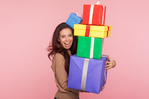 Portrait of cheerful happy surprised woman smiling and shouting in amazement, embracing many gift boxes, enjoying lot of best presents, celebrating birthday. studio shot isolated on pink background