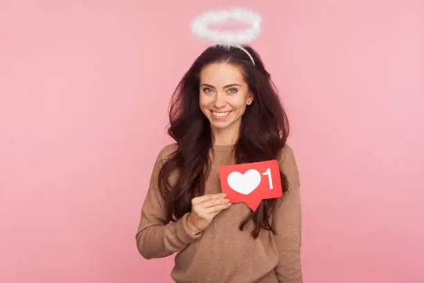 Photo of Social network Heart button. Portrait of optimistic angelic young woman with halo over head holding internet Like icon