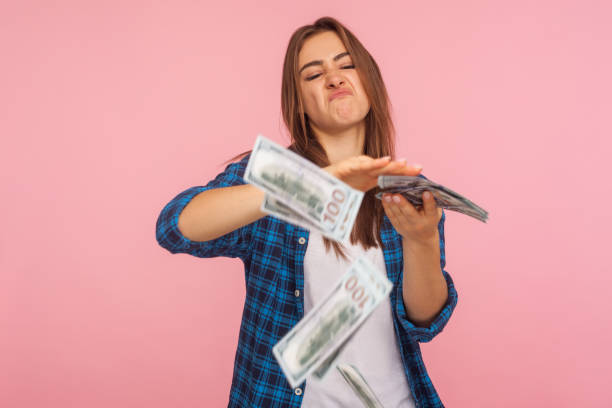 Portrait of wasteful rich girl in checkered shirt scattering dollars with arrogant grimace, boasting wealthy life Portrait of wasteful rich girl in checkered shirt scattering dollars with arrogant grimace, boasting wealthy life, concept of careless money spending. indoor studio shot isolated on pink background careless stock pictures, royalty-free photos & images