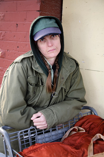 A homeless woman standing on a sidewalk.