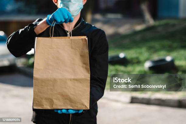 Courier In Protective Mask Medical Gloves Delivers Takeaway Food Employee Hold Cardboard Package Place For Text Delivery Service Under Quarantine 2019ncov Pandemic Coronavirus Covid19 Stock Photo - Download Image Now