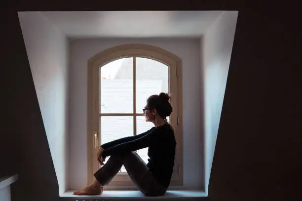 Photo of Isolated woman worried looking through the window at home.