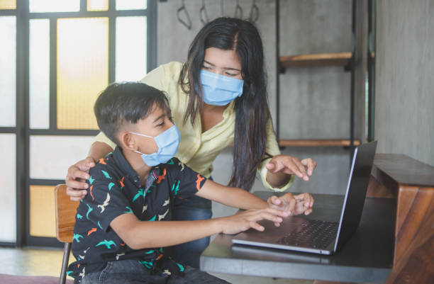 istock Lockdown and school closures. Mother helping her child with face mask studying online classes at home. Quarantine, self-isolation, online education concept, home schooler during COVID-19 pandemic 1218811609