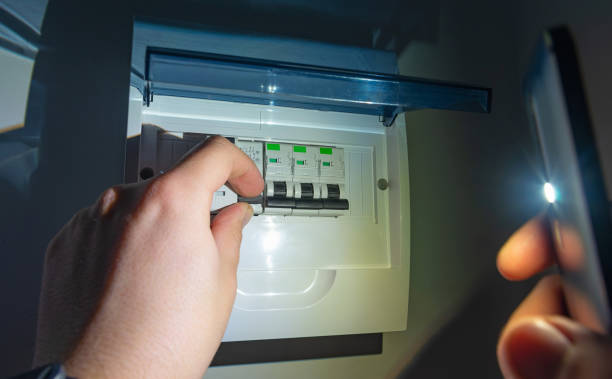 A man in complete darkness, is using a smartphones flashlight to investigate and switches ON residual current device (RCD) consumer unit in an automatic fuse box during a electric power outage at home. Blackout, short circuit, concept. A man in complete darkness, is using a smartphones flashlight to investigate and switches ON residual current device (RCD) consumer unit in an automatic fuse box during a electric power outage at home blackout photos stock pictures, royalty-free photos & images