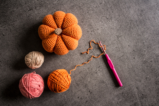 Crochet pumpkin, hook and cotton yarn balls on dark grey background. Top view photo. Hobby