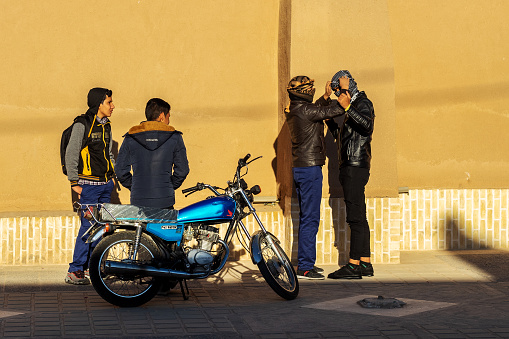 Four guys are standing near a motorcycle. Two of them hide their faces by wearing a headscarf Keffiyeh. Youth in Islamic Republic of Iran.