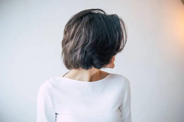 A young beautiful girl with short dark hair who turned away from the camera and shows her new hair styling.