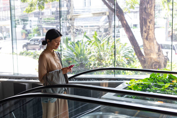 istock Staying Connected: Happy Asian Woman Texting on her Mobile Phone While Riding an Escalator 1218822046