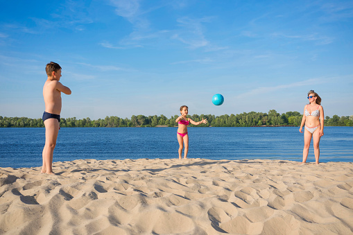 The family plays volleyball on the sand, on a sunny bright day.  Sport games.