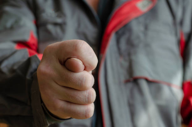 A man shows a fig gesture to the camera. Mechanic in red-gray working uniform with a gesture of cookies. Conflict in the workplace. Close-up. Selective focus.