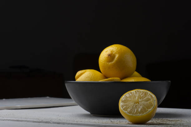 istock Yellow lemons in a black bowl, on a white wooden table. 1218822183