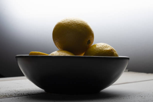 Yellow lemons in a black bowl, on a white wooden table and black background.