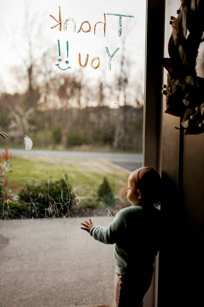 Bambino alla porta della tempesta di vetro che si guarda fuori: il vetro ha scarabocchi per bambini e messaggio di ringraziamento - foto stock